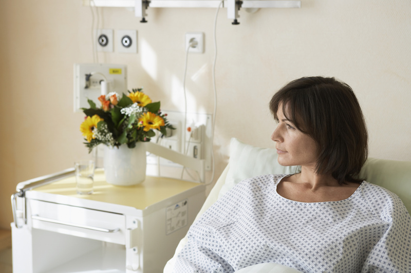 Sick woman in hospital bed with flowers on bedside table