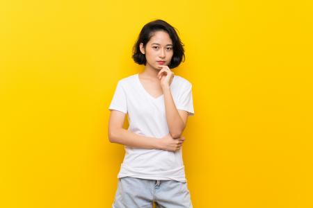 Woman wondering if breast augmentation is permament against yellow background