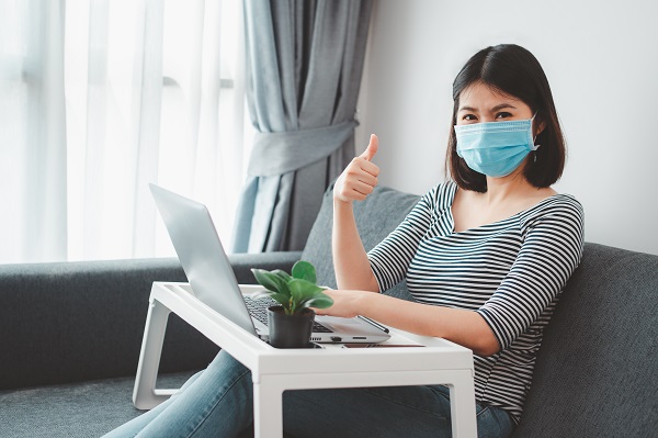 Woman in facemask, sitting on a couch, using a laptop, planning an estate
