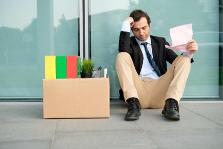 fired businessman slumping against office building reading termination notice